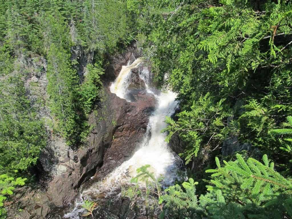 A summer version of the same falls with the left side clearly disappearing into a black rock hole.