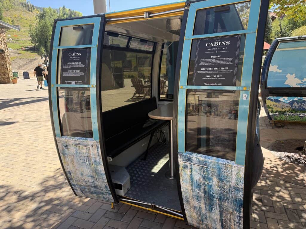 A single detached gondolacabin with the doors open and a table and two benches inside.  Instructions on the outside say they can be used on a first come, first served basis.