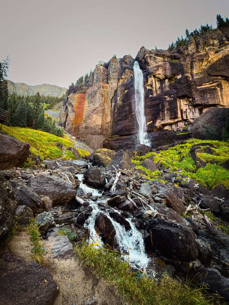 Bridal Veil Falls plummeting from the high, sheer cliff to a pool below, and then flowing out across the rocky creek-bed below.