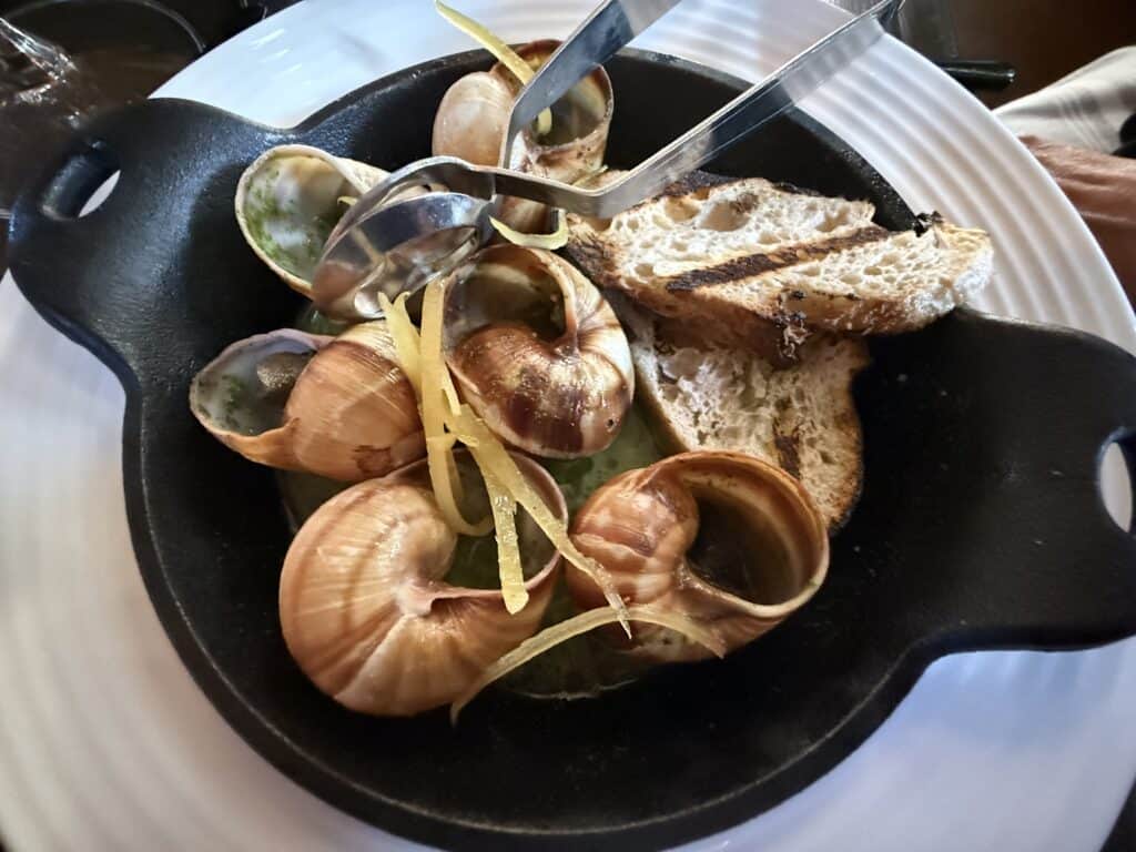 Six escargot with baguette slices in a cast iron dish.