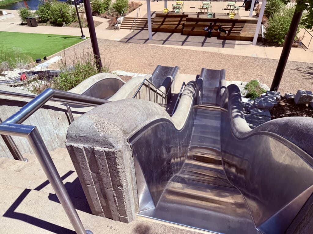 Two steep slides sit side by side, with 2-foot concrete walls on either side of each slide.  A staircase runs between them to climb back up.