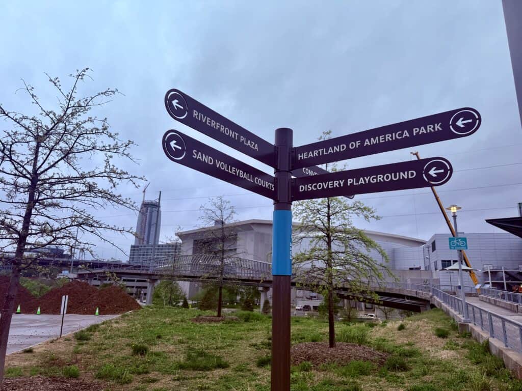 Signs point in different directions to the riverfront, a park, volleyball courts, and the playground.
