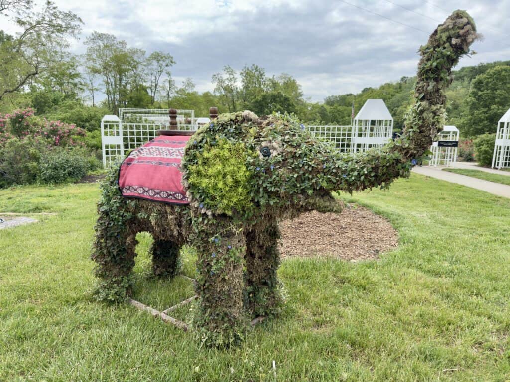 A large elephant is built of greenery.  Its trunk is lifted high in the air.
