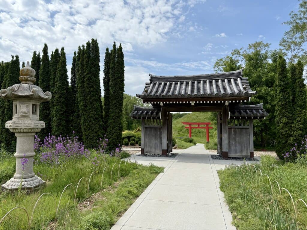 The Japanese Gardens with flowers and trees, a gazebo, and in the distance a red arch shaped in what appears to be a Japanese letter.