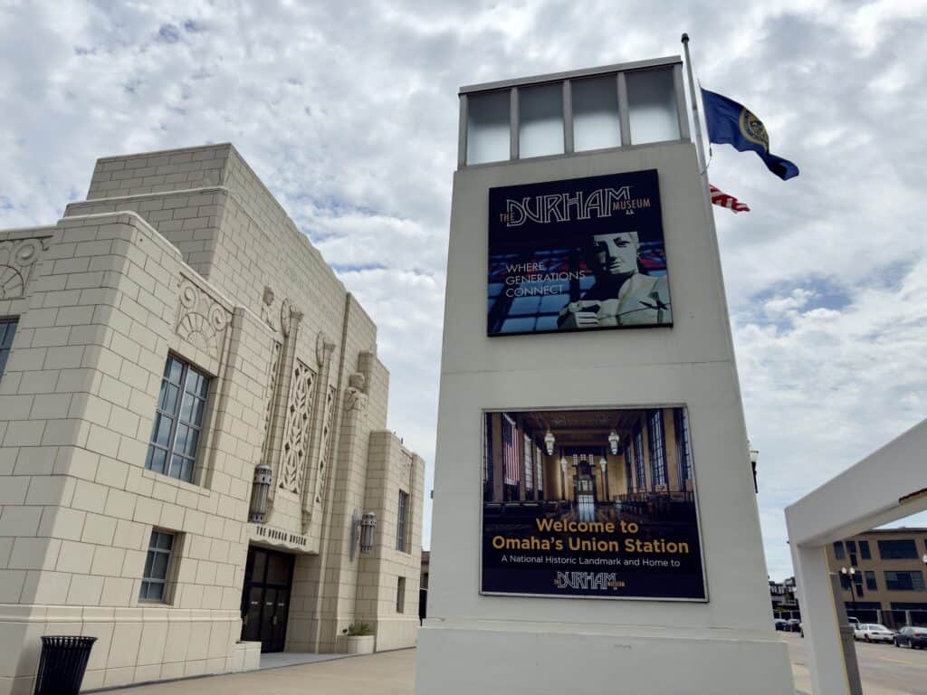 A two story stand-alone wall has a sign for the Durham on top, and a sign saying "Welcome to Omaha's Union Station" on the bottom.