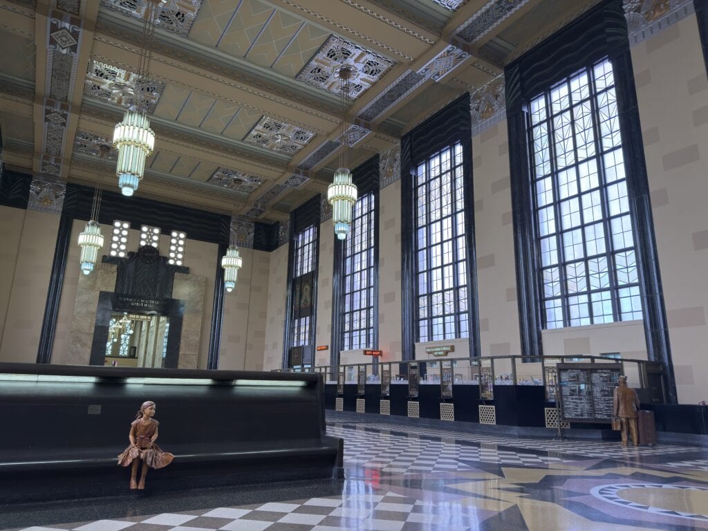 In the Great Hall, a bronzed statue of a salesman stands looking at the schedule, and a statue of a little girl sits on a bench.