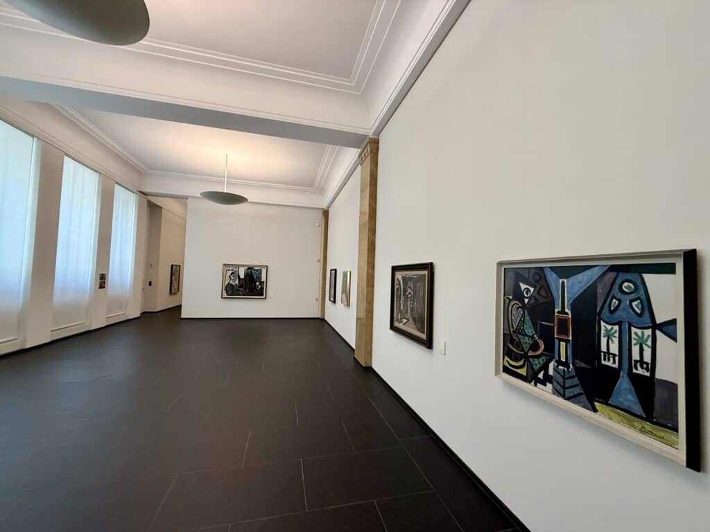 A room of the gallery with the walls lined with brightly colored paintings by Picasso.