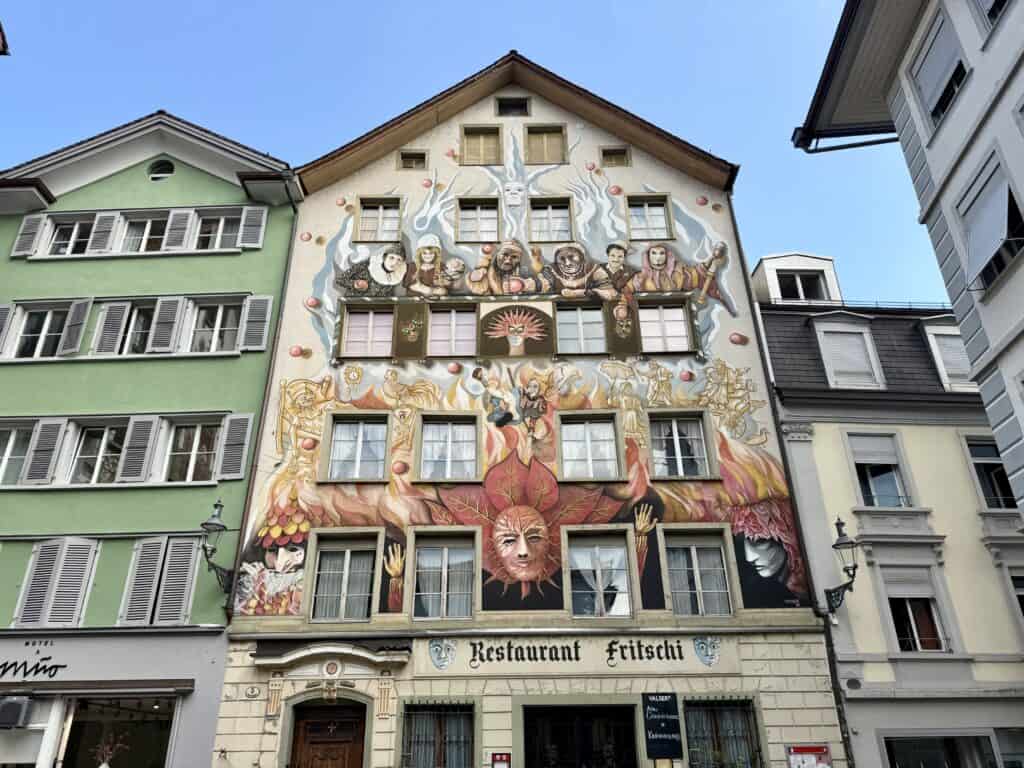 A 6+ story building is decorated on all stories with bright red and yellow Mardi-gras style murals.  The first floor has a banner for Restaurant Fritschi.