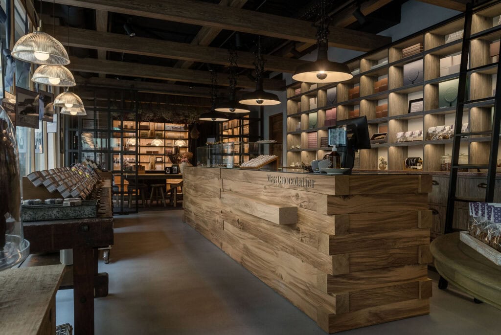 Artistically lit interior of chocolate shop with rustic counter area made of wood beams, and shelves of chocolate.