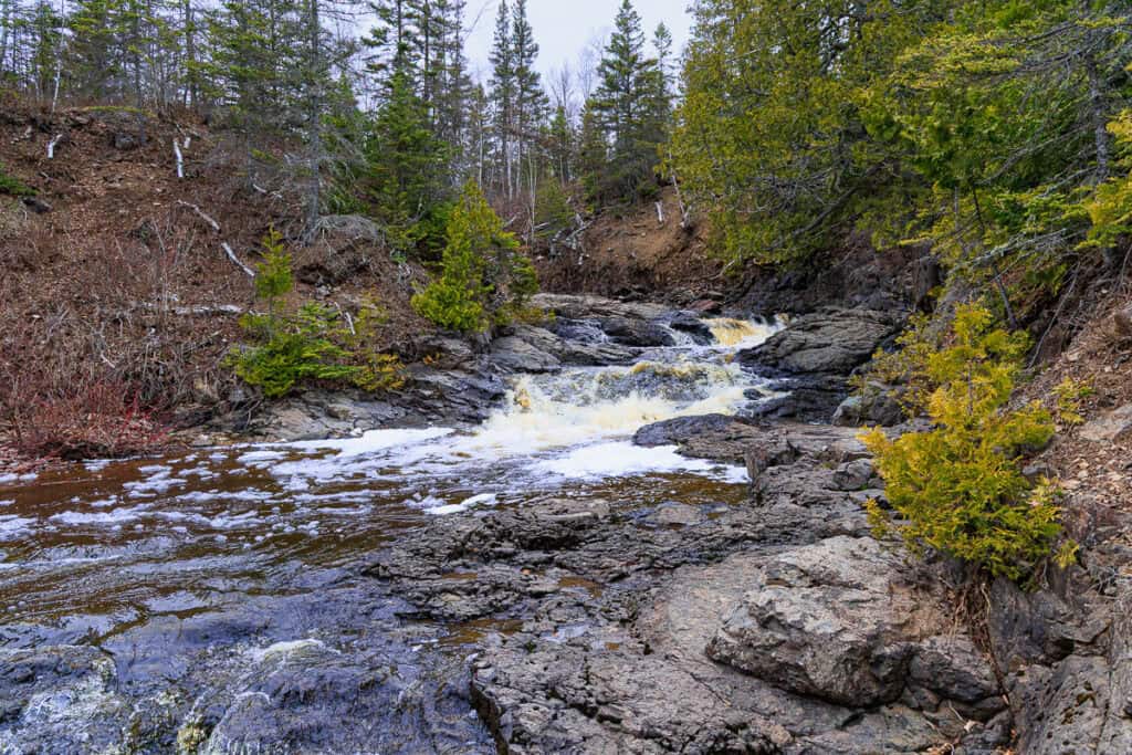 Walking along the riverbed lined with trees and ledge rock.