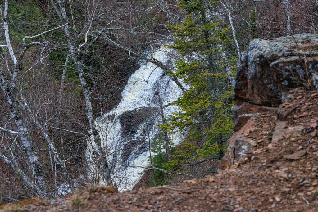Peeking through the trees and over a rocky ledge at part of a very long waterfall below.