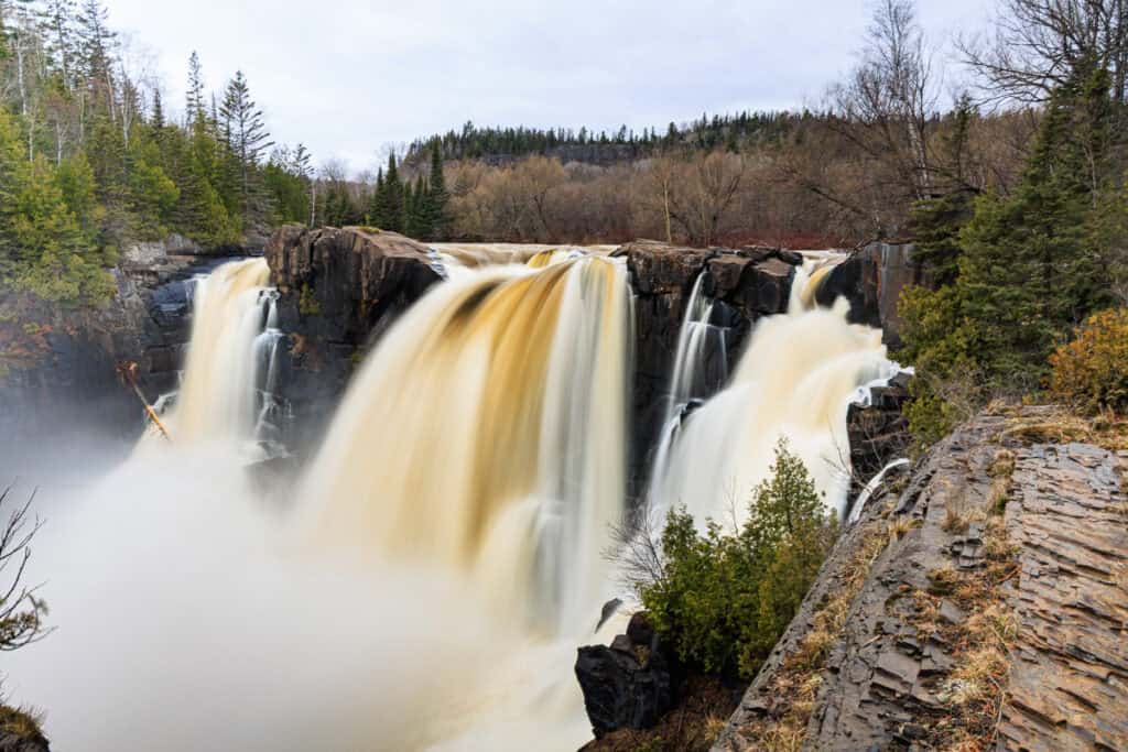 The Canadian side of the falls with at least six different streams of the falls visible.  The Pigeon River above it is visible and you can see it fallling over the cliff.