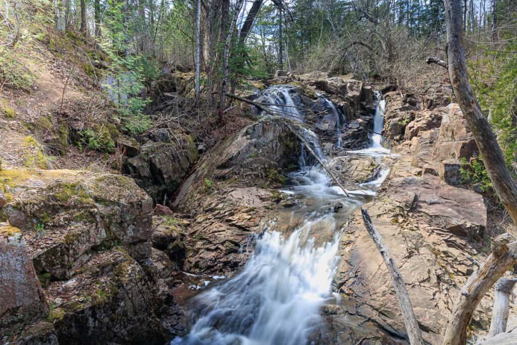 Three waterfall streams join into one, tumbling down over rocks into a pool below.