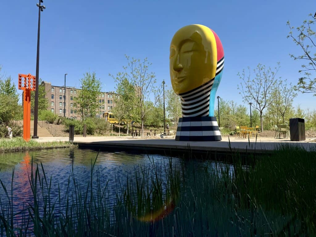 A sculpture of a huge yellow face with a black and white striped neck sits at the edge of the water.