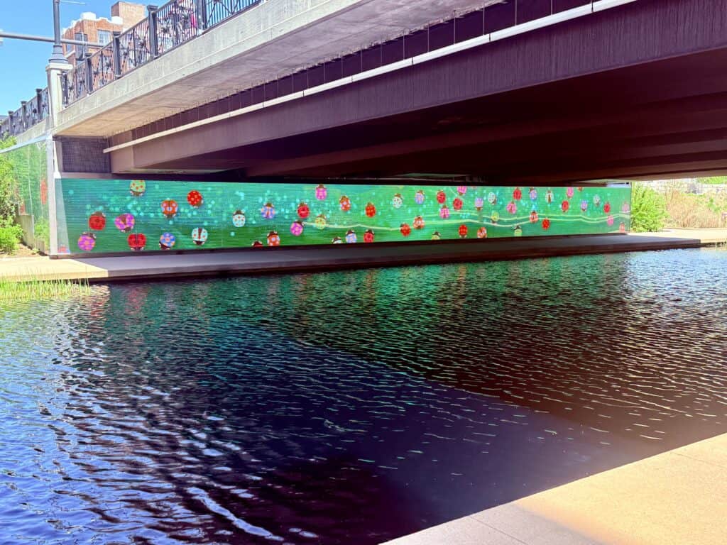 A tunnel under a street bridge with a red, yellow, and green colored display of ladybugs.