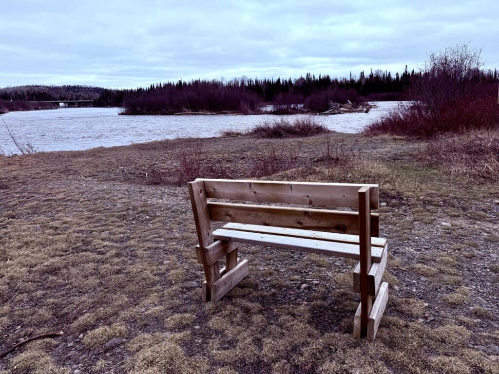 A bench sits with a view of the calm, quiet Pigeon River, downstream from the falls.