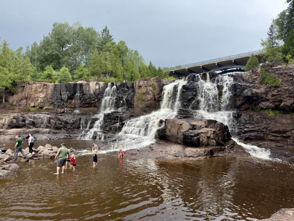 Middle Falls at Gooseberry Park with a dozen or so adults and children playing in the water below.