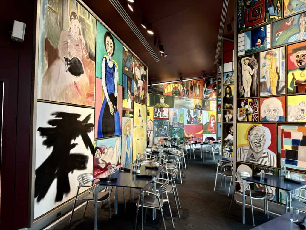 Dozens of brightly colored paintings displayed in different sizes in the cafe, with tables and chairs lining the walls.