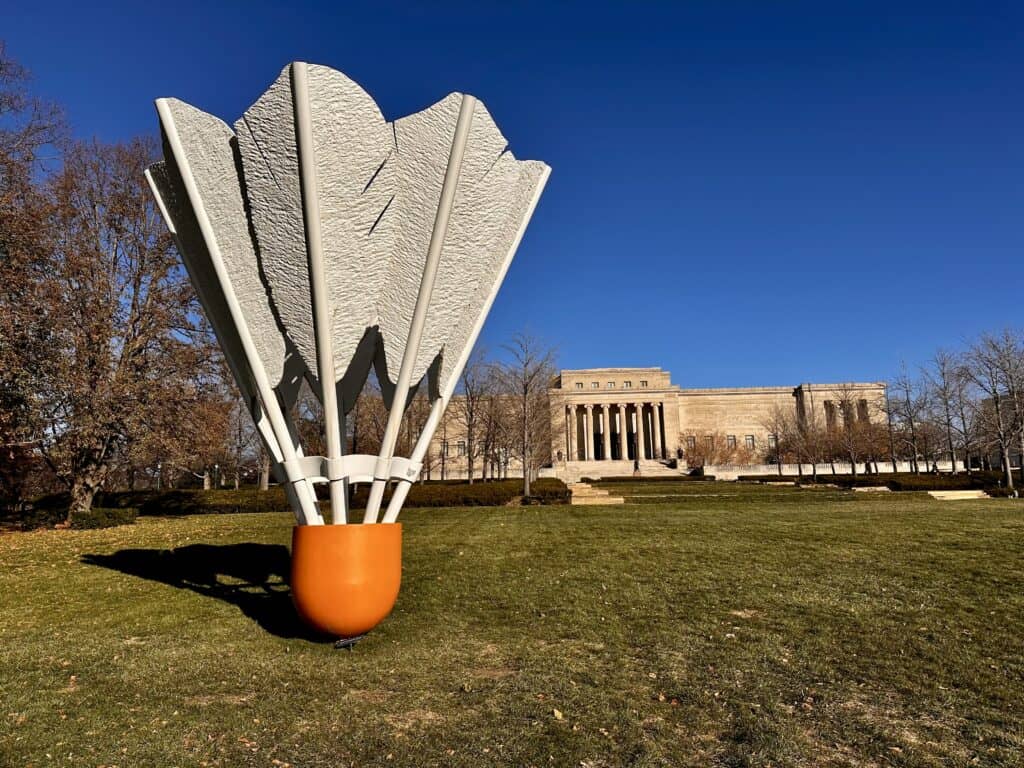 A giant shuttlecock standing straight up with its nose on the ground. The Nelson-Atkins Museum is in the background.