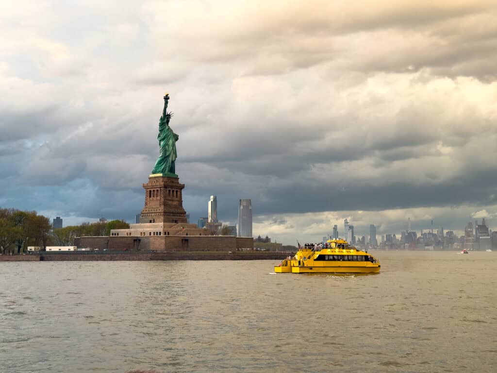 Symbol of the United States: The Statue of Liberty under stormy clouds, with a tourism boat passing by
