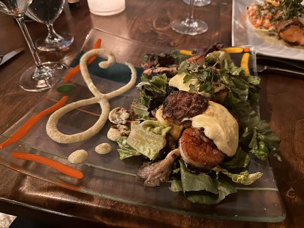Salad with seared scallops. Sauce is artistically drizzled on the glass plate.